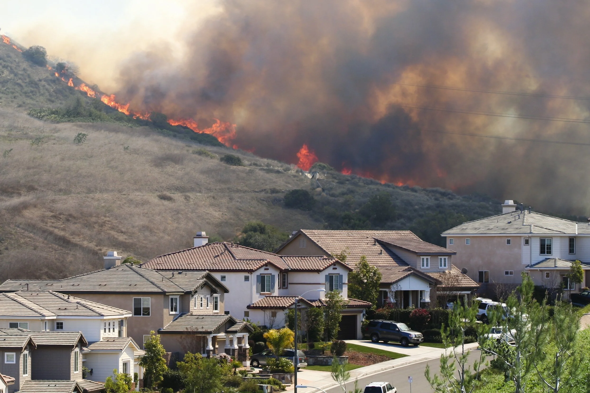 Residential neighborhood adjacent to a hillside on fire with dense smoke and flames visible.