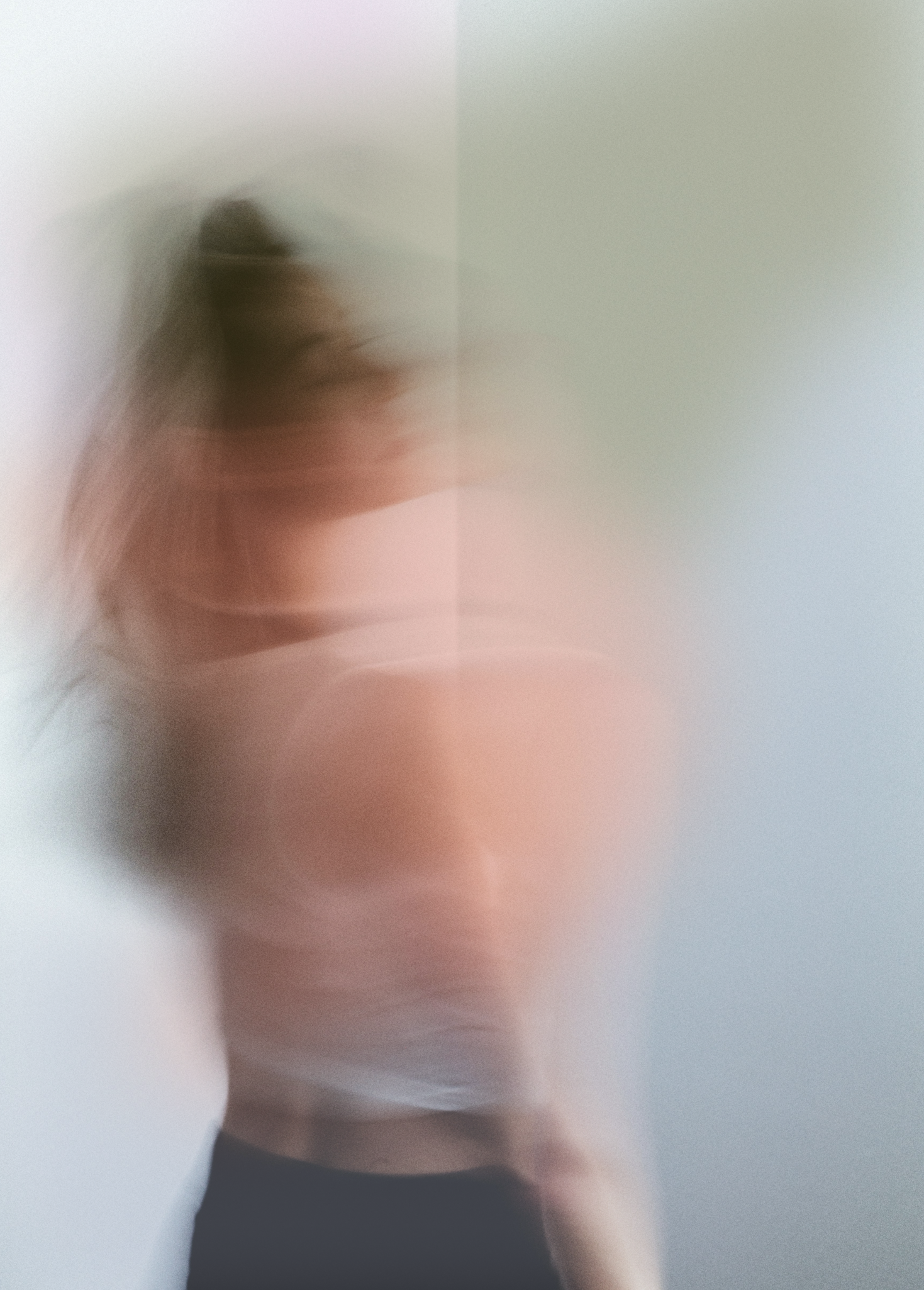 A blurry, abstract photo of a woman with long hair in motion, standing against a plain wall.