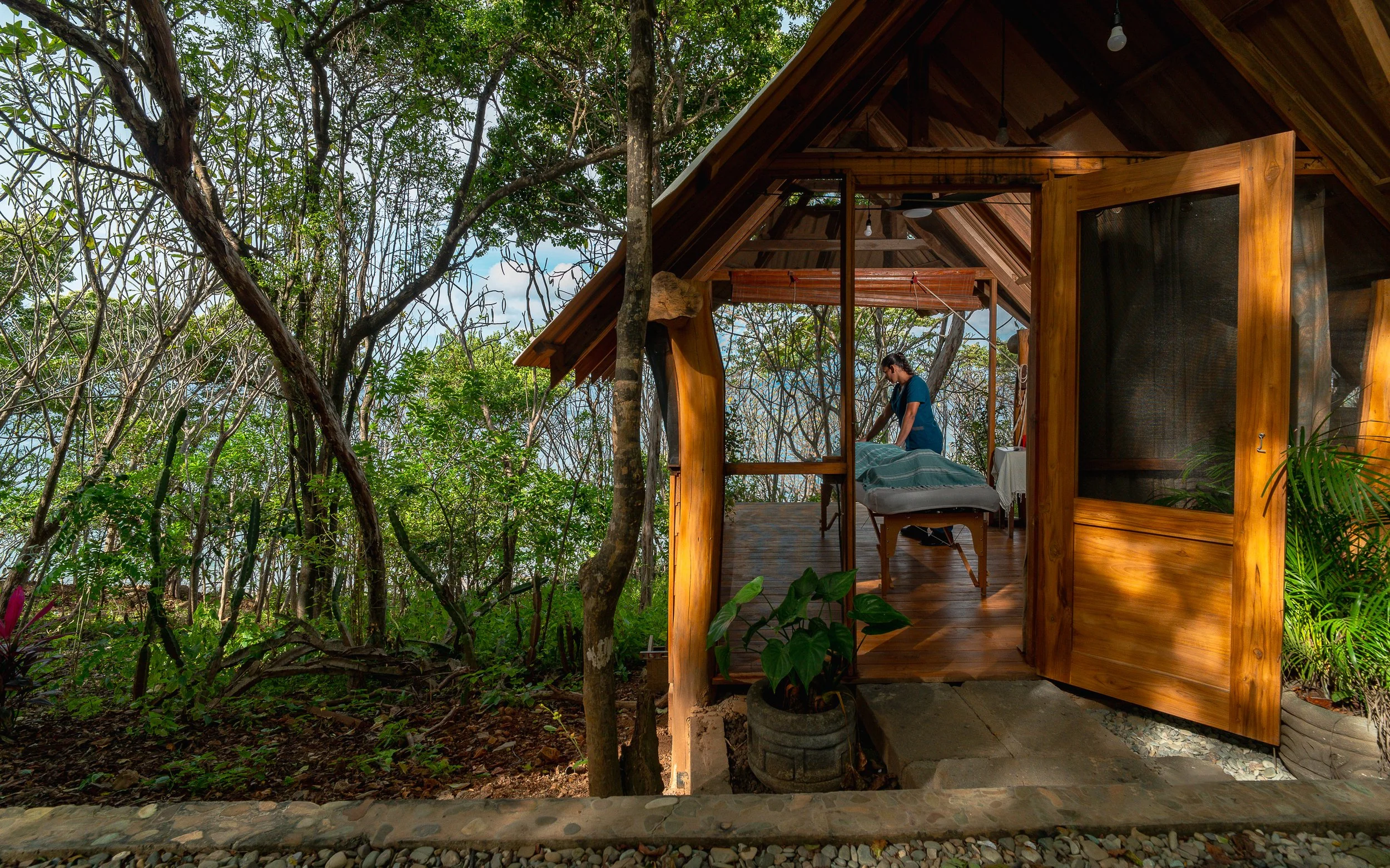 A person inside a wooden  massage cabin surrounded by trees in a forest.