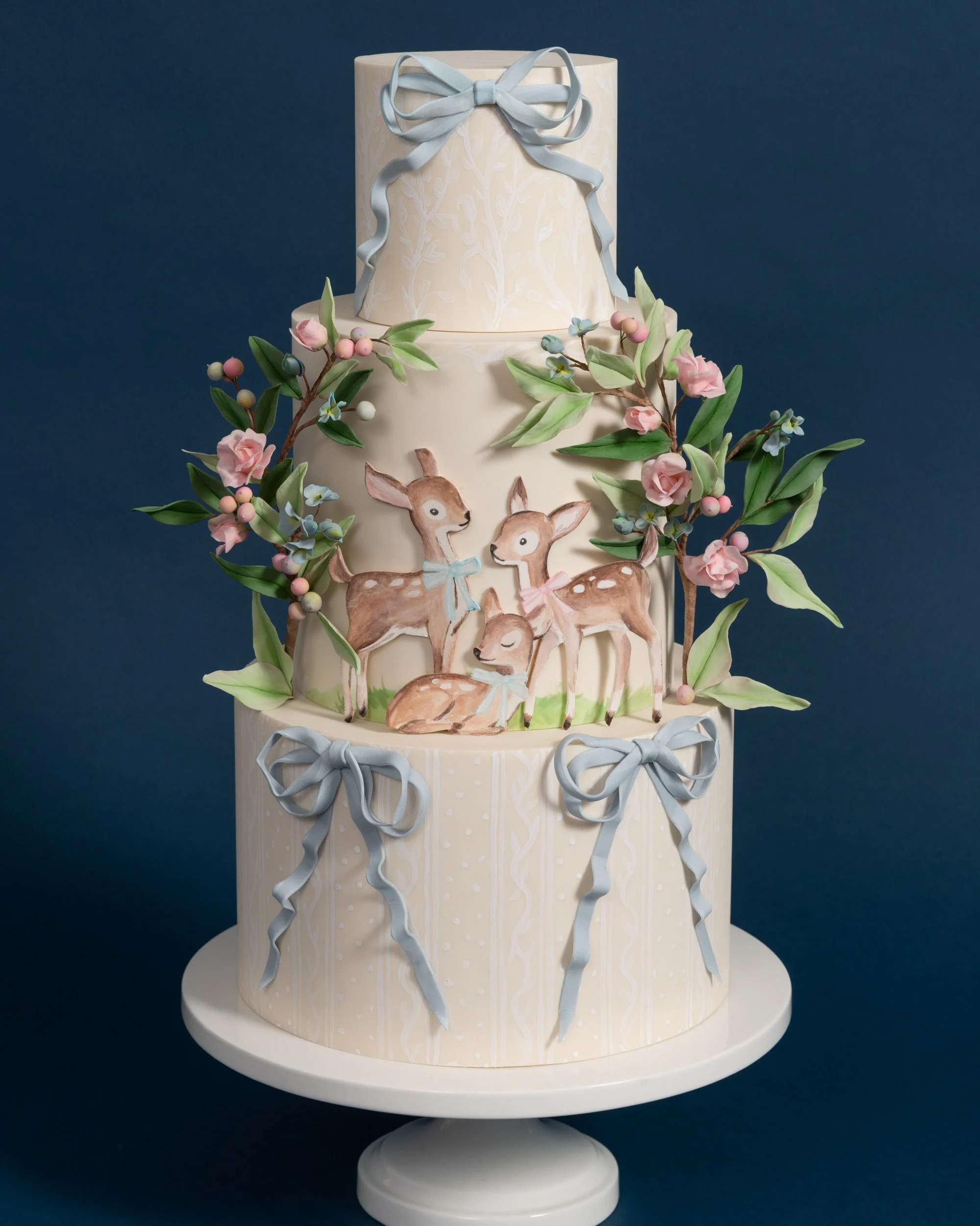Baby shower cake with blue ribbons, roses, and a family of deer