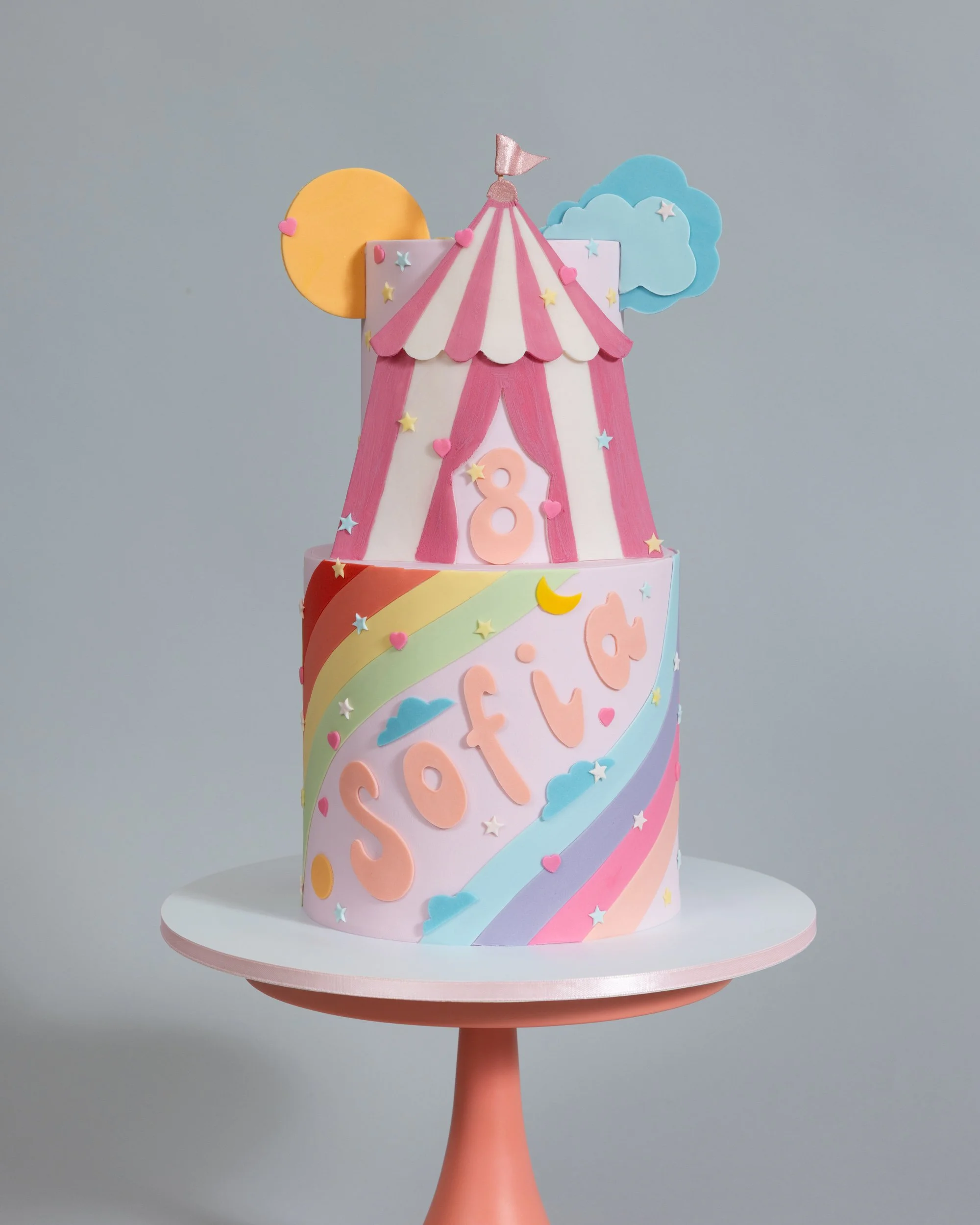 Pretty pink circus tent birthday cake with rainbow, sun and clouds