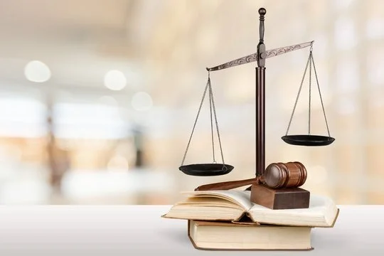 A balanced scale and gavel placed on an open book, with additional stacked books underneath, symbolizing law and justice.