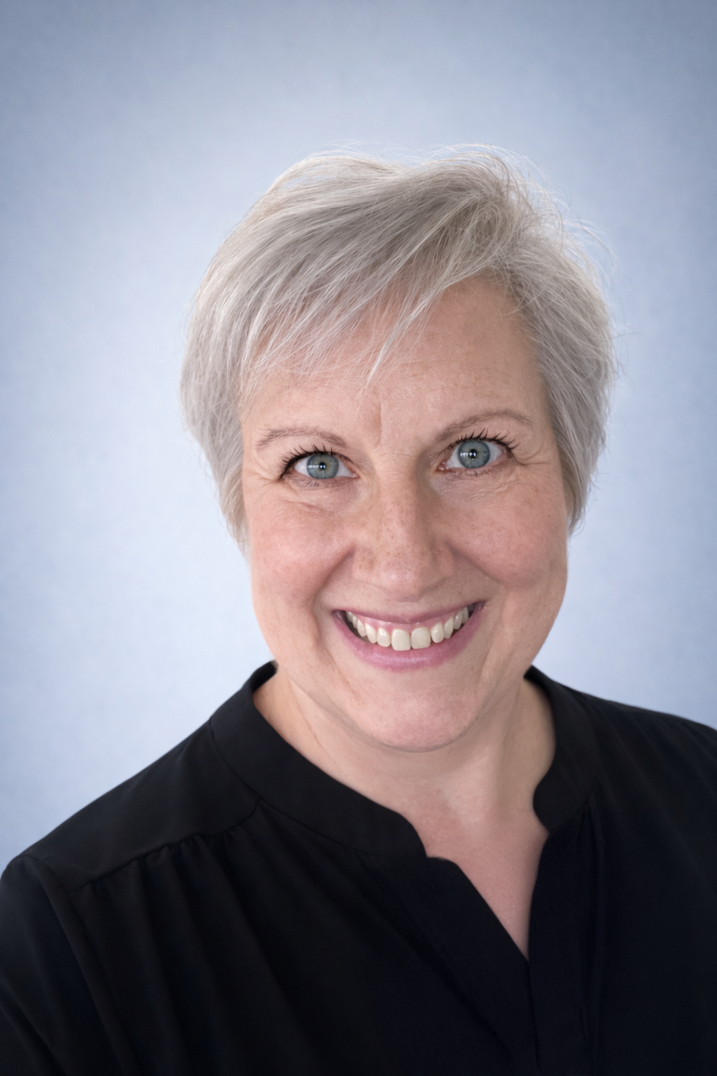 A middle-aged woman with short gray hair smiling at the camera with a light blue background.