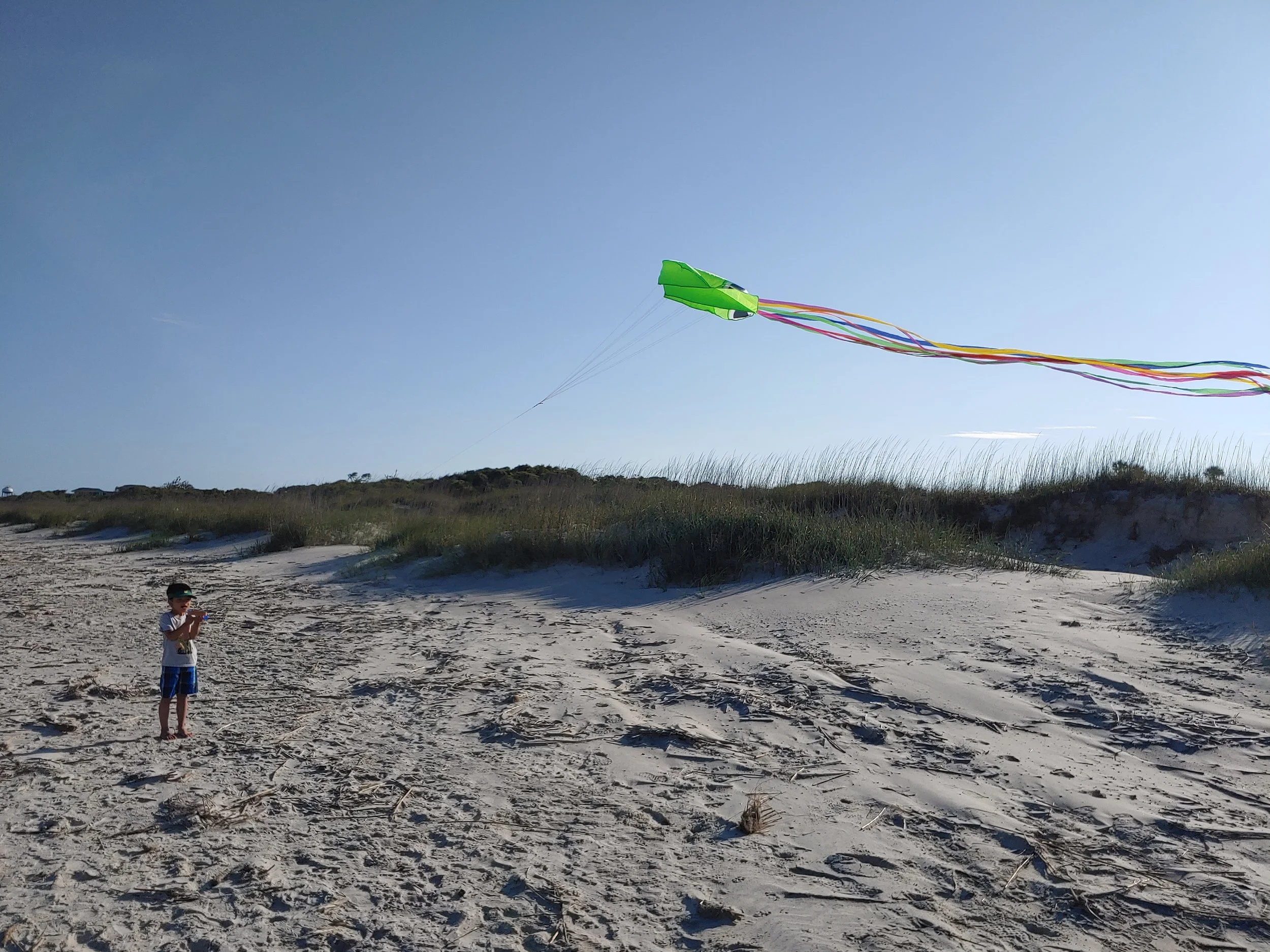 A child standing on a sandy beach flying a colorful kite in the sky.