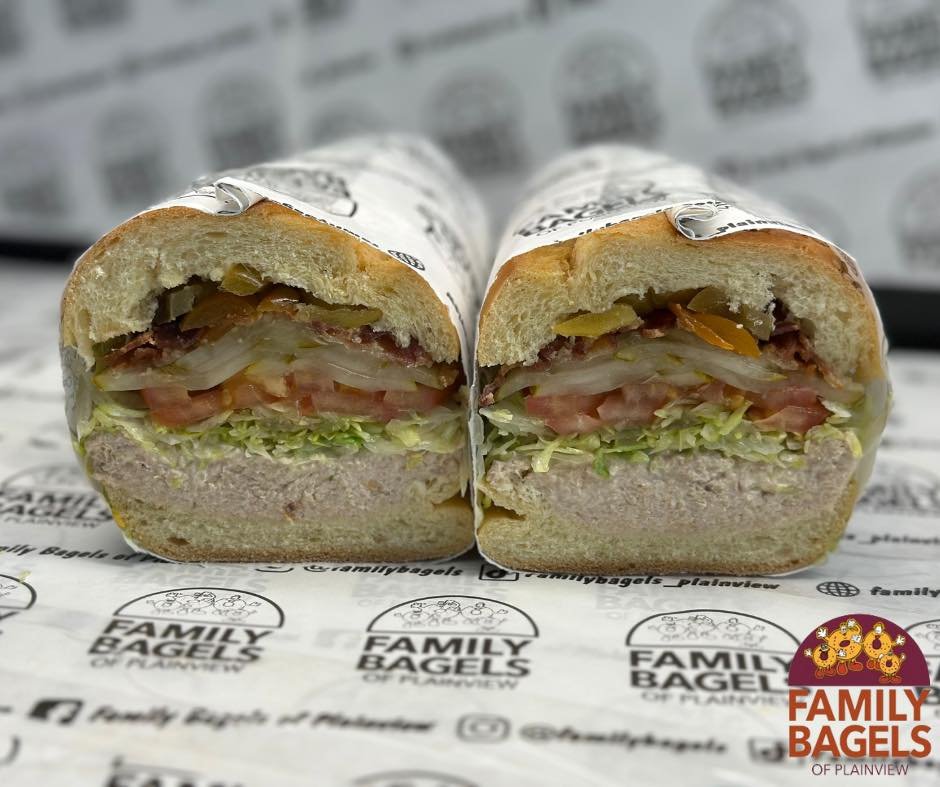 Cross-section of a submarine sandwich with lettuce, tomato, pickles, ham or turkey, and cheese in a sandwich bun.
