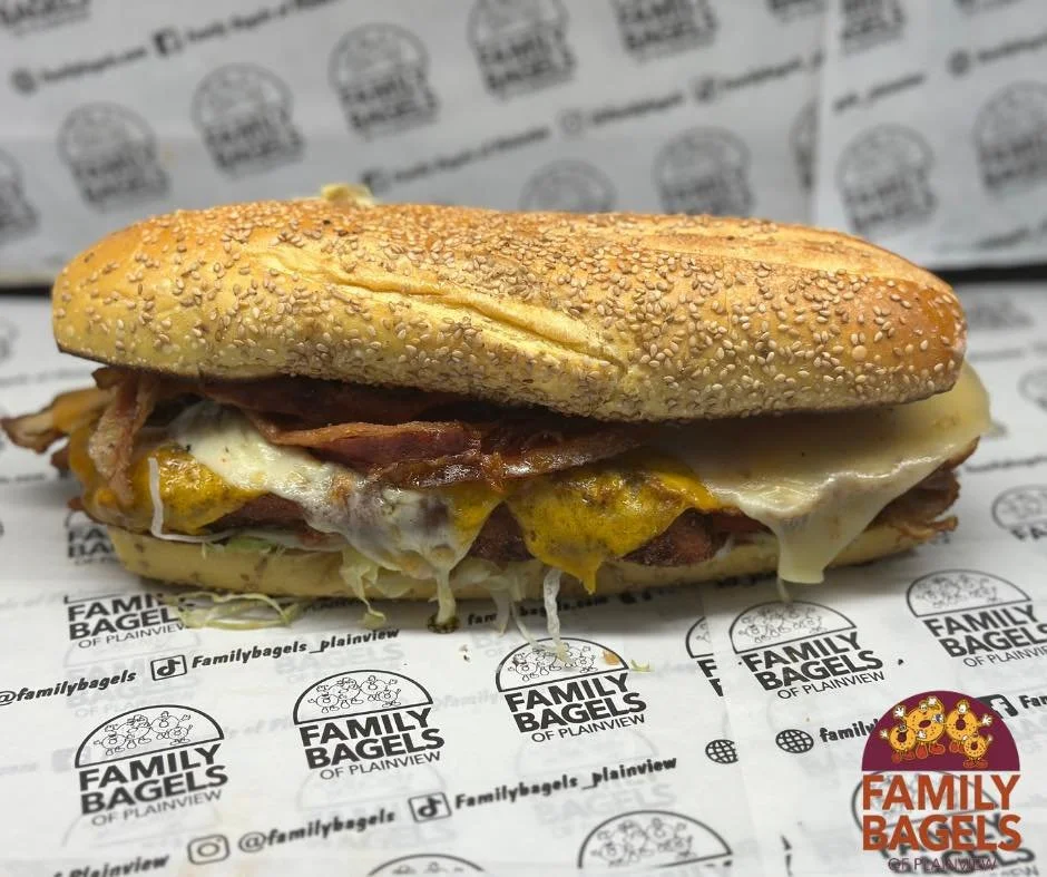 A sandwich with sesame seed bun, bacon, fried egg, and cheese, placed on paper with Family Bagels branding.