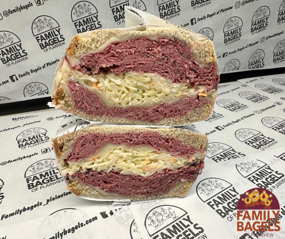 A sliced pastrami and cheese sandwich on wheat bread with cole slaw inside, placed on branded paper from Family Bagels of Plainview.