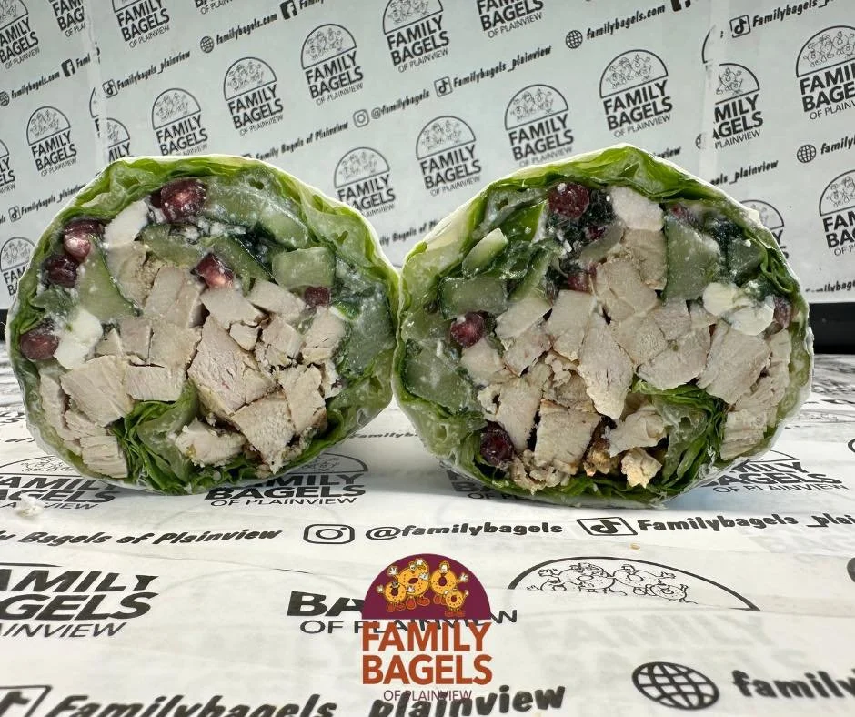 Cross-section of a chopped salad wrap with pieces of chicken, leafy greens, and pomegranate seeds inside a green lettuce wrap.