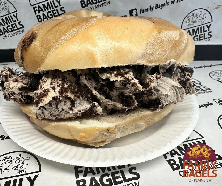 Ice cream sandwich with chocolate and vanilla cookies, served on a white paper plate lined with paper printing 'Family Bagels of Plainview'.