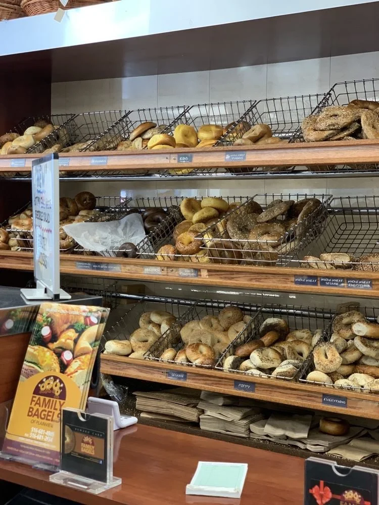 Display of various fresh bagels on wire racks at a bakery counter.