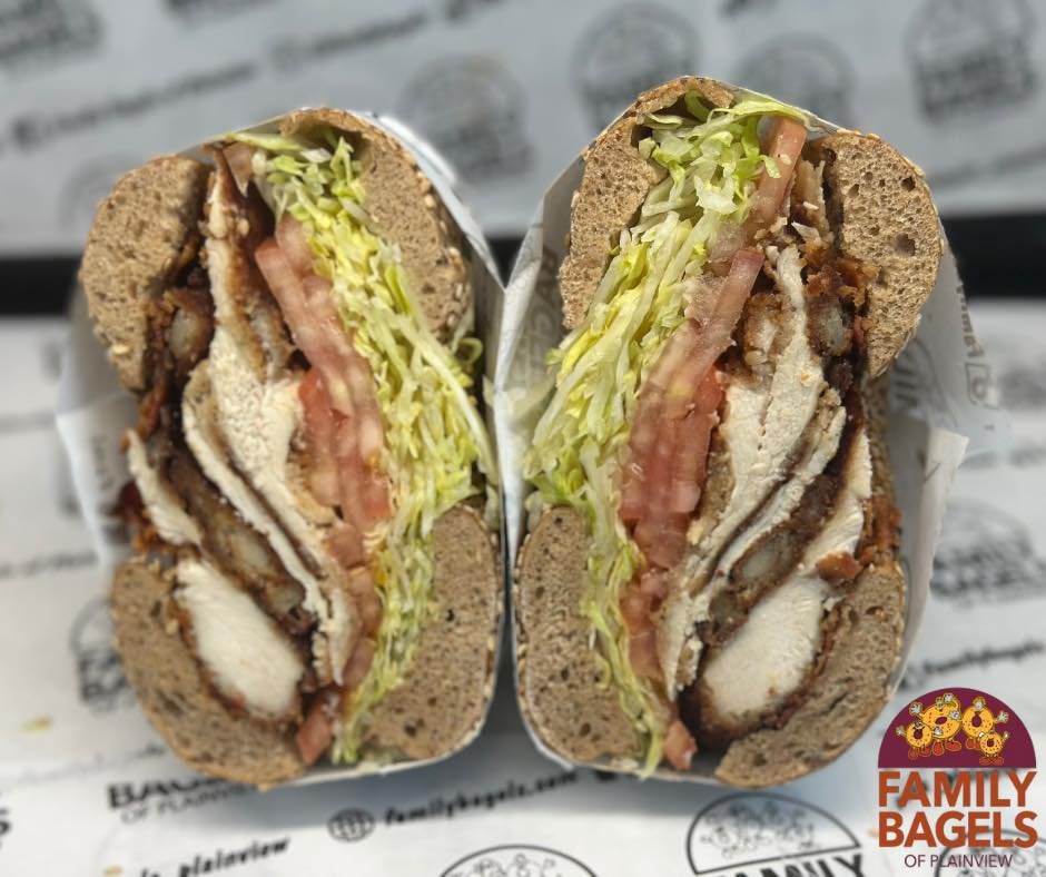 Cross-section of a bagel sandwich with lettuce, tomato, turkey, bacon, and various fillings, wrapped in paper with Family Bagels branding.