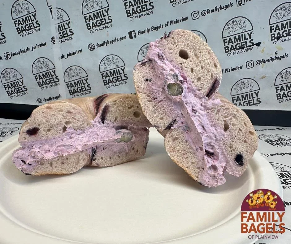 Two half slices of bagel with pink berry cream cheese filling on a white plate, with a background featuring a pattern of logos for Family Bagels of Plainview.