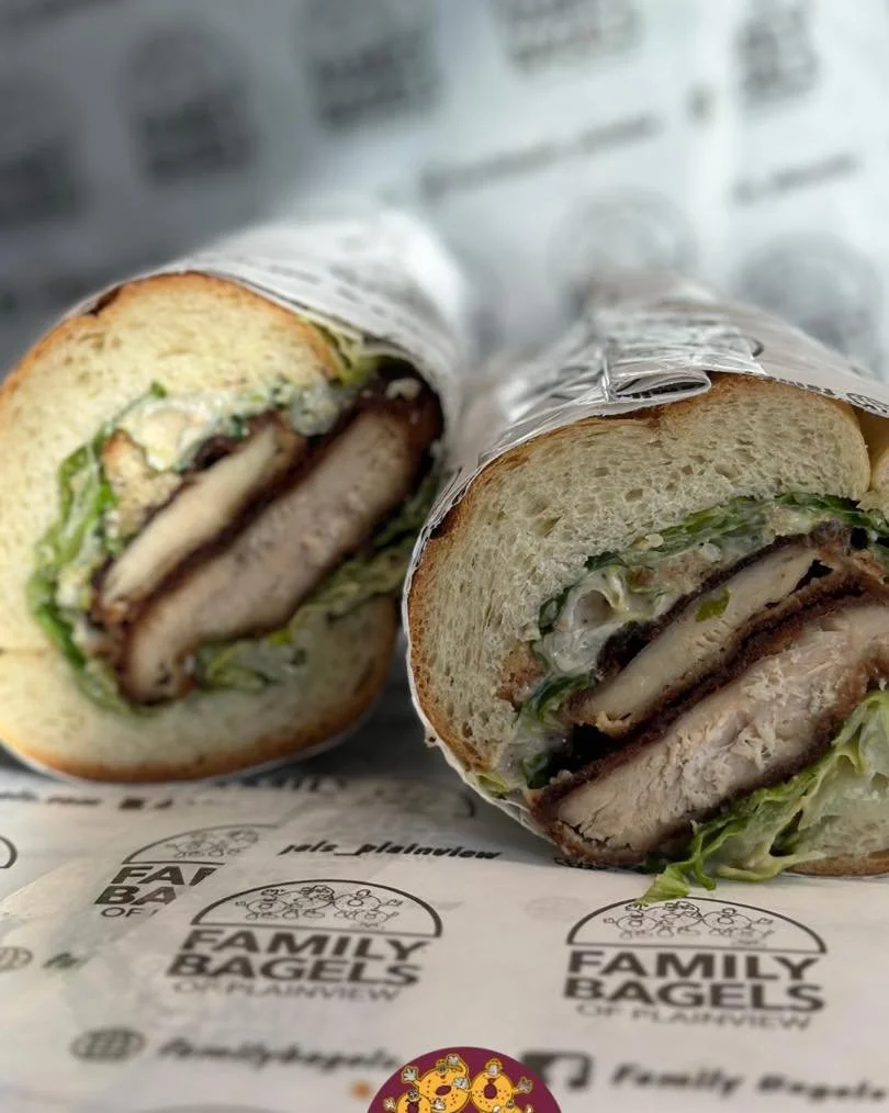 Cross-section of a sandwich with bread, lettuce, turkey, cheese, and condiments, wrapped in branded paper from Family Bagels.