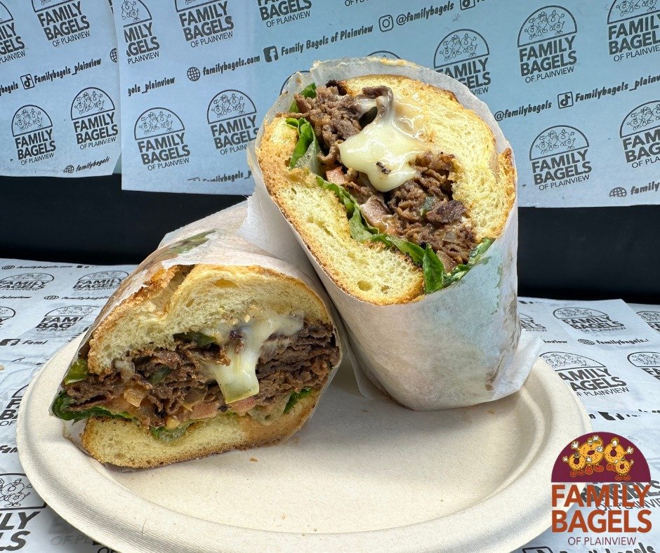 A cut beef and cheese sandwich wrapped in paper, on a white plate, with a background of branded paper and logo for Family Bagels.