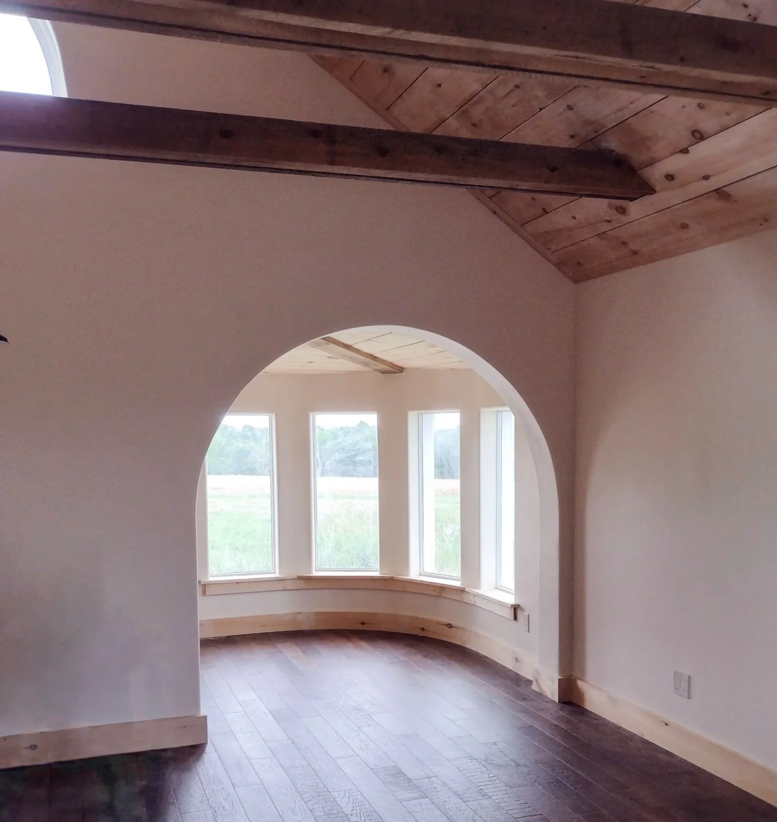 Interior of a room with wooden ceiling, curved wall with large windows, and dark hardwood flooring.