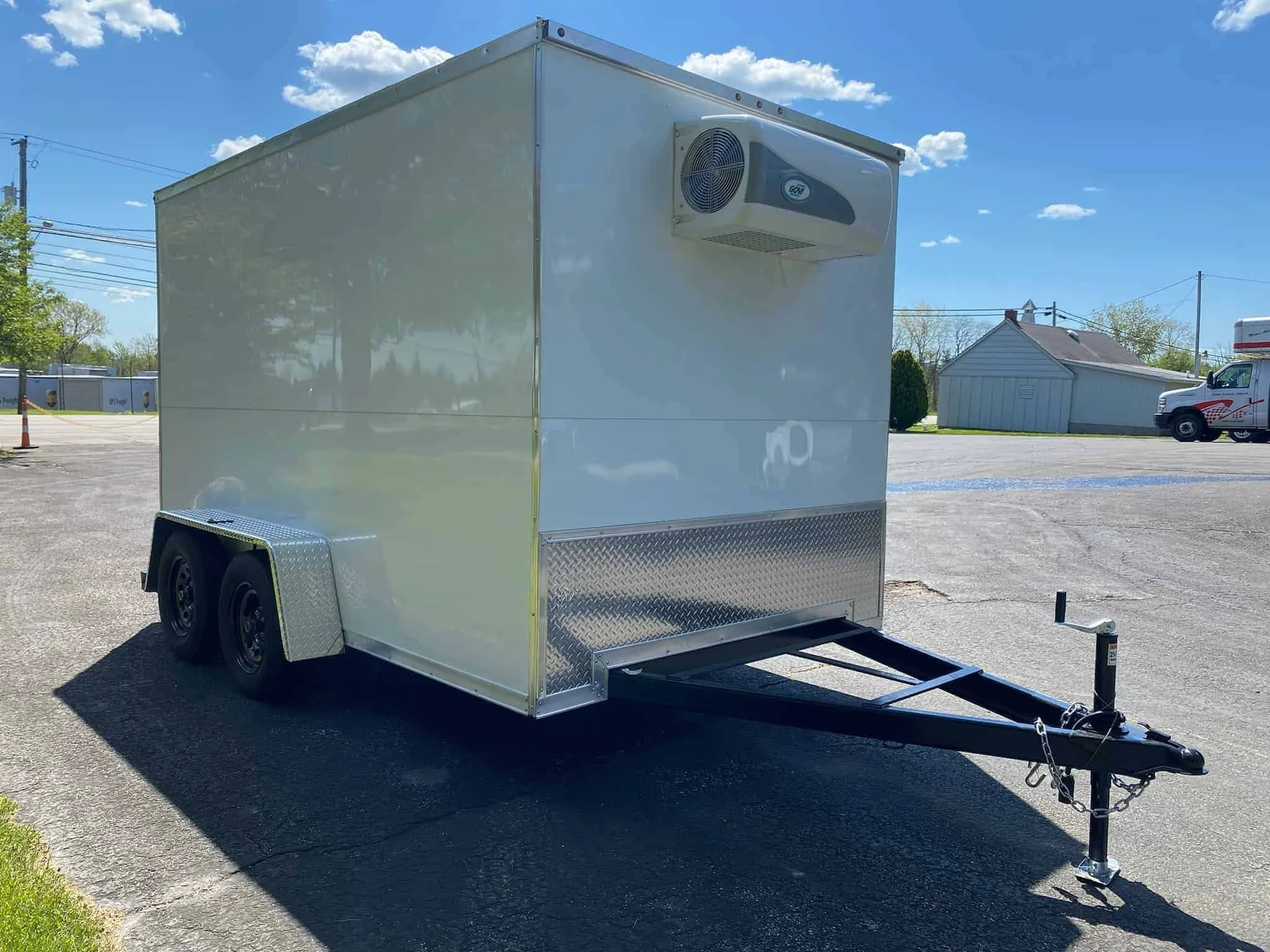 A white mobile food trailer with a refrigerated air conditioning unit attached to the front, parked on a paved lot under a clear sky.