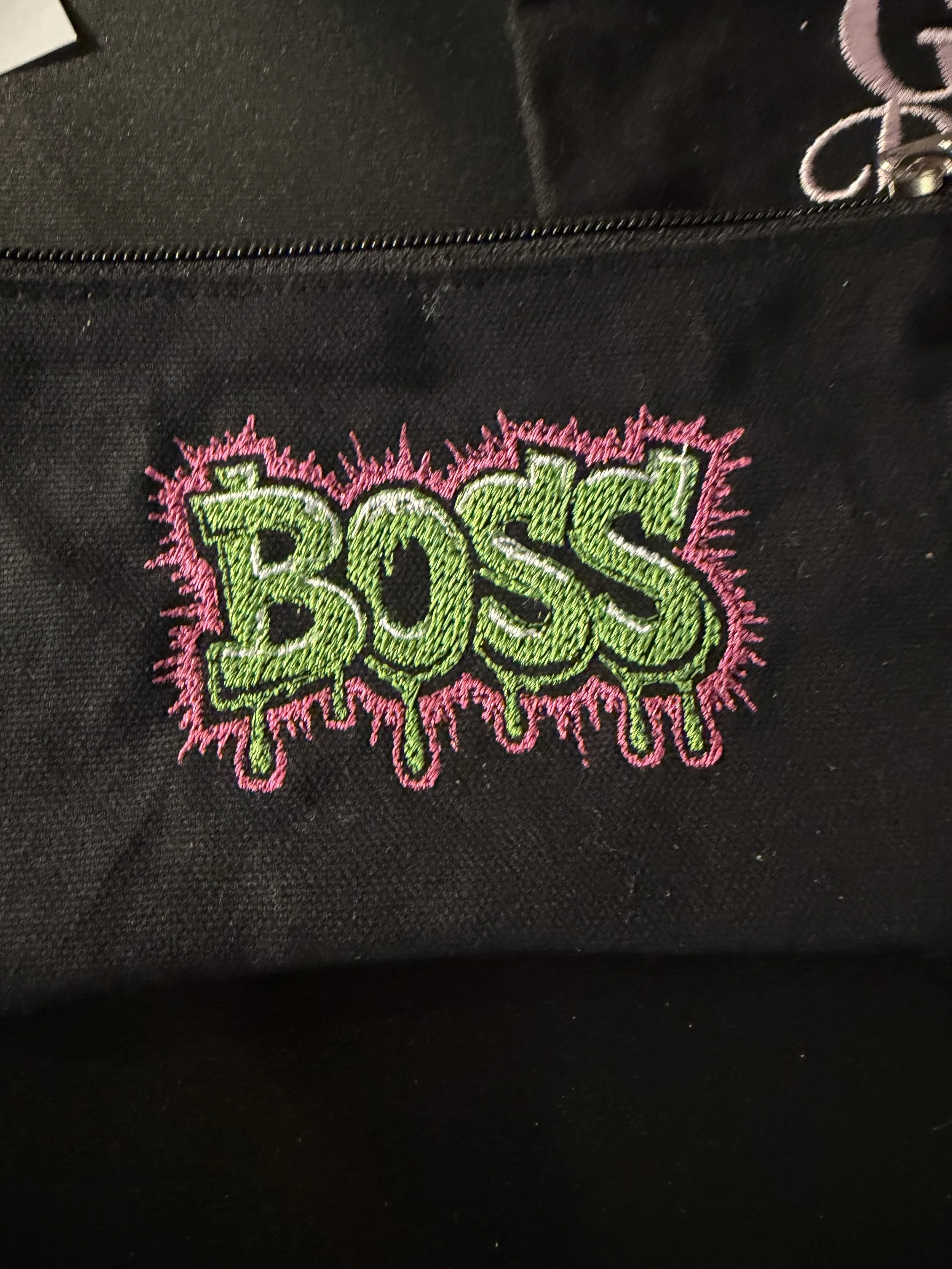 Close-up of black fabric with colorful embroidered design that reads 'BOSS' in green with pink outline and accents.