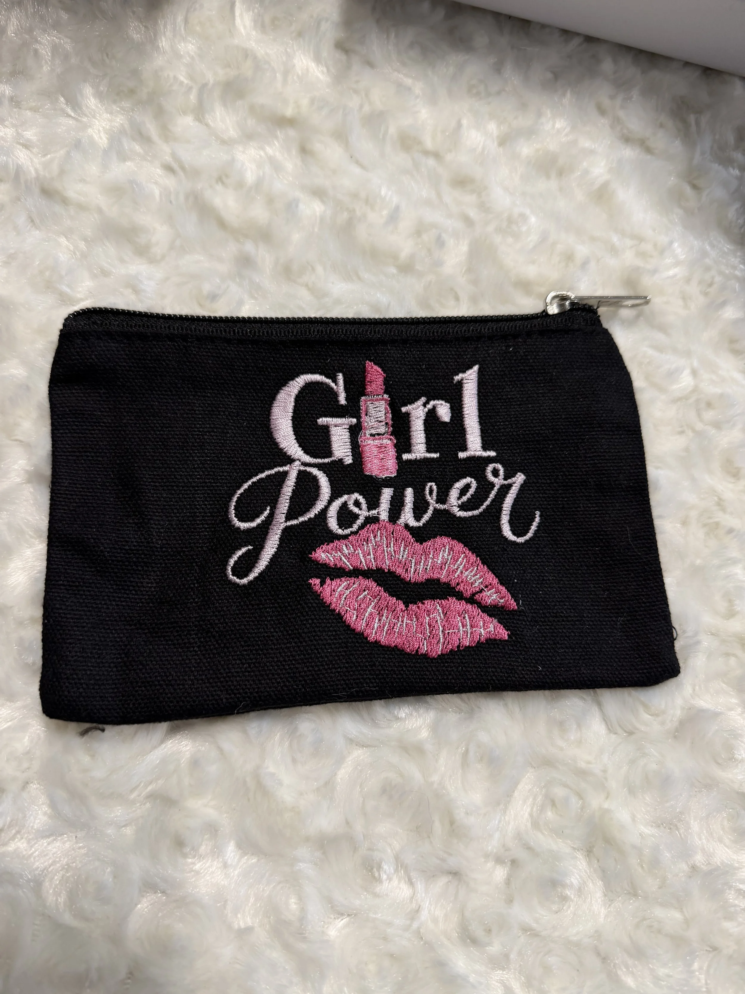 A black fabric pouch with pink embroidered lips and the words "Girl Power" featuring lipstick and lipstick lipstick