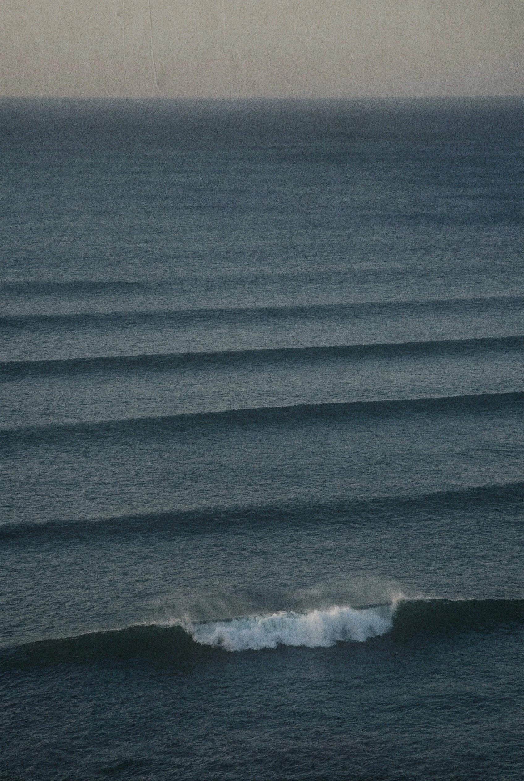 Photo of ocean waves with white foam and dark water, under a cloudy sky.