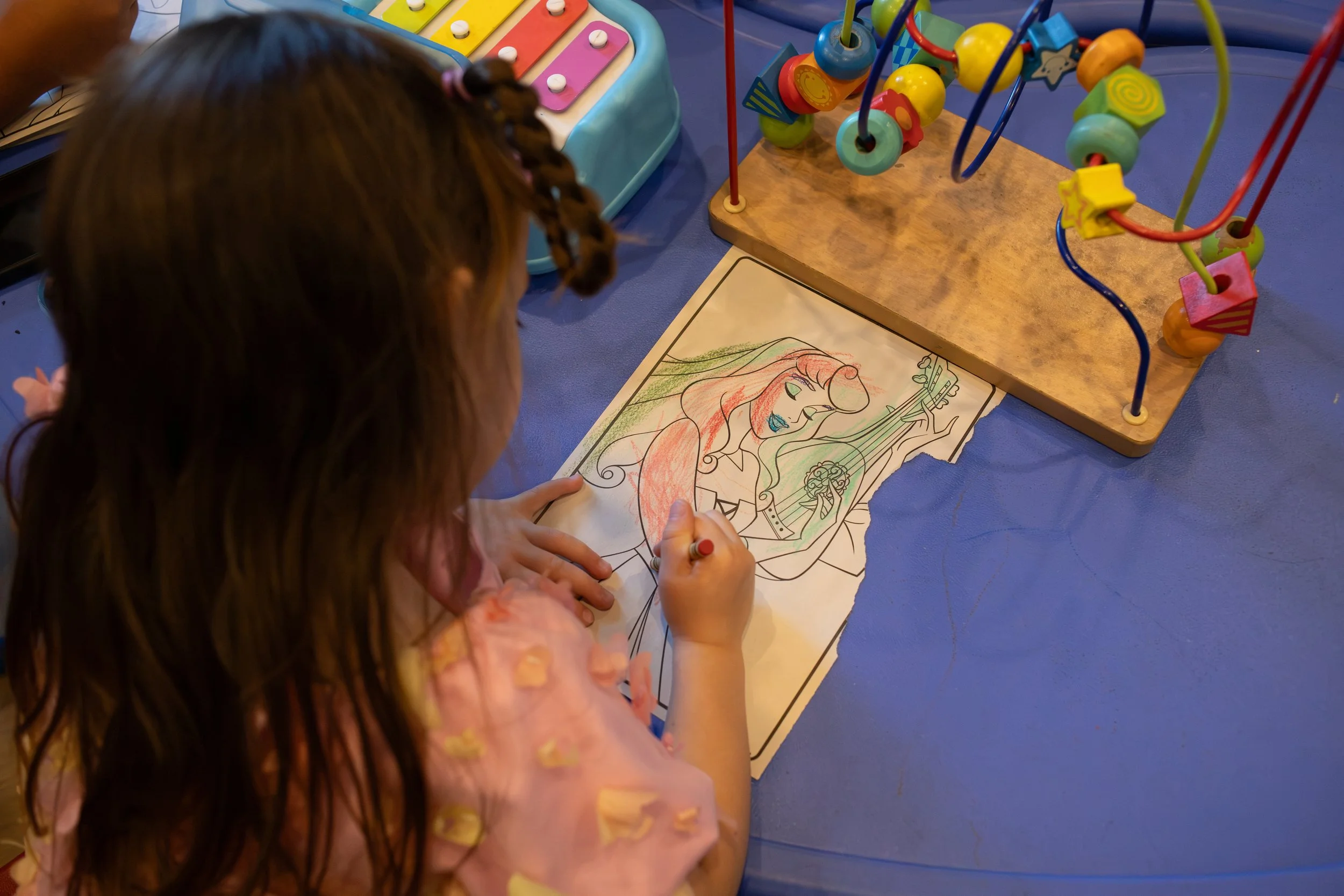 A young girl with braided hair coloring a picture of a woman with long, flowing hair, possibly a princess or fairy tale character.