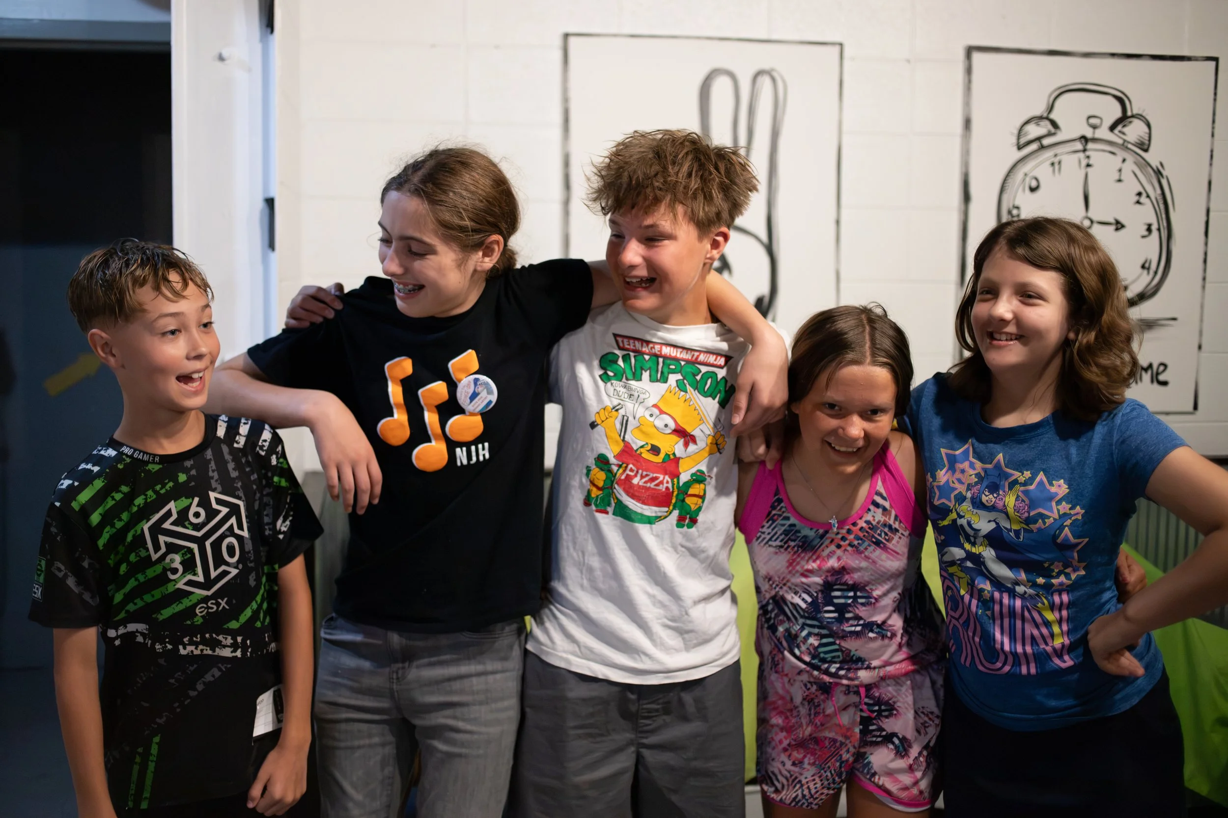 A group of six children smiling and hugging each other indoors.