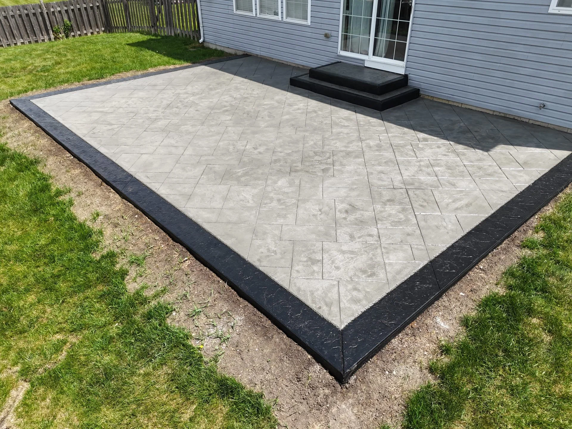 Stamped concrete patio with 2 steps and a dark stamped border detail around both steps and the patio itself.