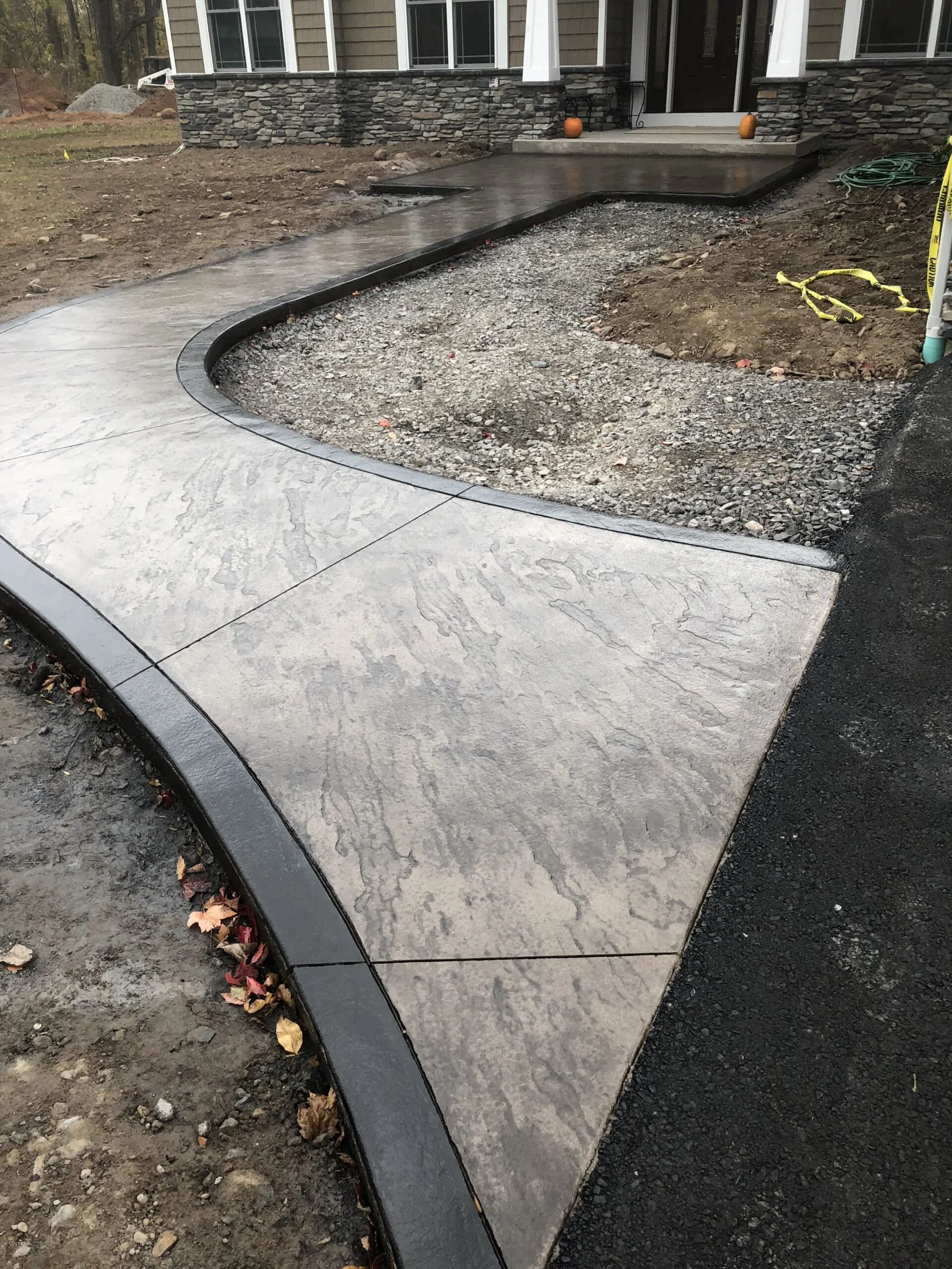 Stamped slate walkway with grey color and dark border leading from paved driveway to front porch