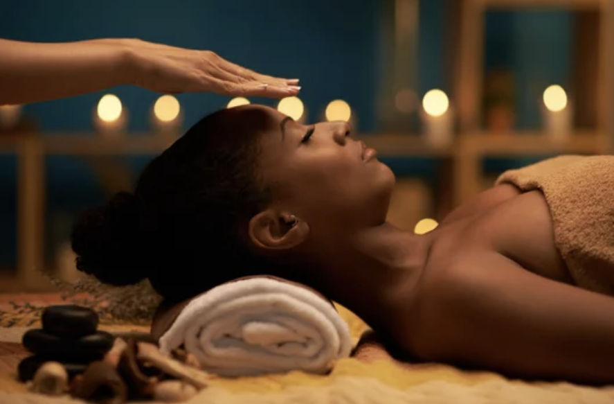 A woman receiving a massage in a spa, lying face up with a rolled towel under her neck, candles in the background