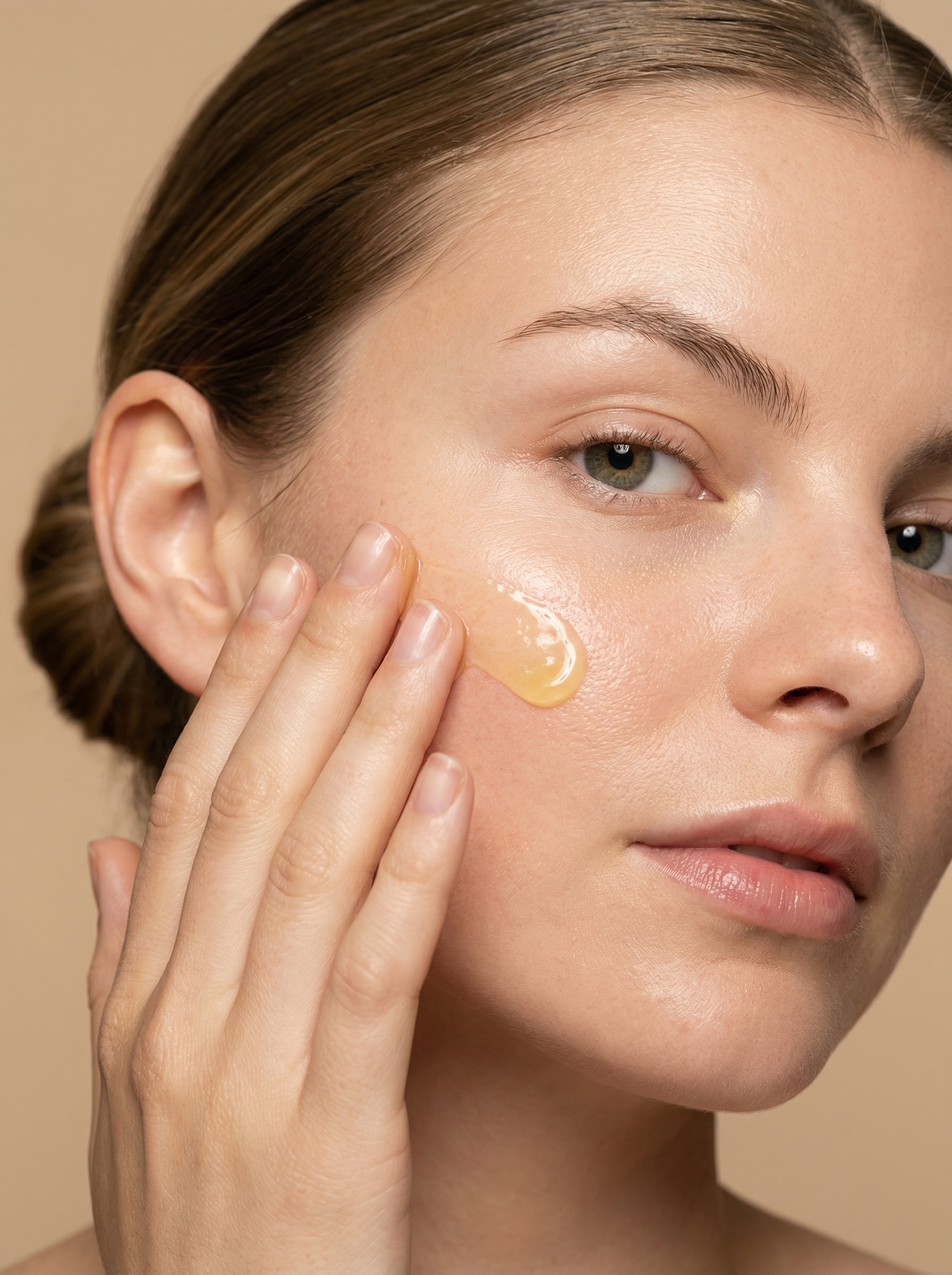 Close-up of a woman with brown hair applying a gel skincare product to her cheek using her fingers.