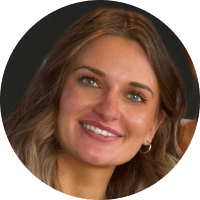 Close-up of a smiling young woman with long, wavy brown hair and blue eyes, wearing a dark top.