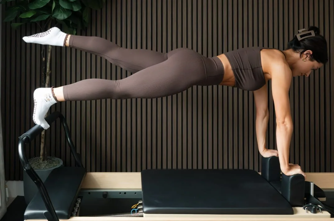 Woman performing a plank exercise on a Pilates reformer machine in a fitness studio.