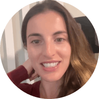 Close-up of a smiling woman with long, wavy brown hair, wearing a red top, indoors.