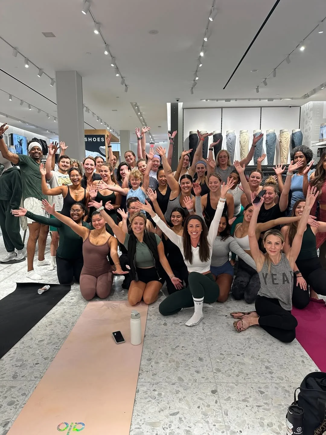 Group of people in a fitness class inside a store, smiling and raising their hands in celebration.