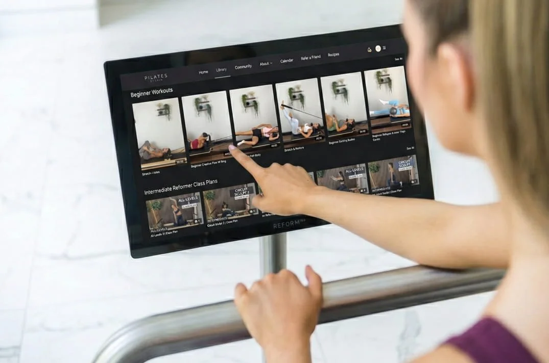 A person selecting a beginner Pilates workout video on a digital screen.