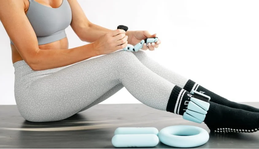 Person sitting on the floor, assembling workout equipment, with foam rollers and resistance bands nearby.