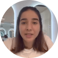 A young woman with long dark hair and light skin, looking at the camera, in an indoor setting with a bright background.