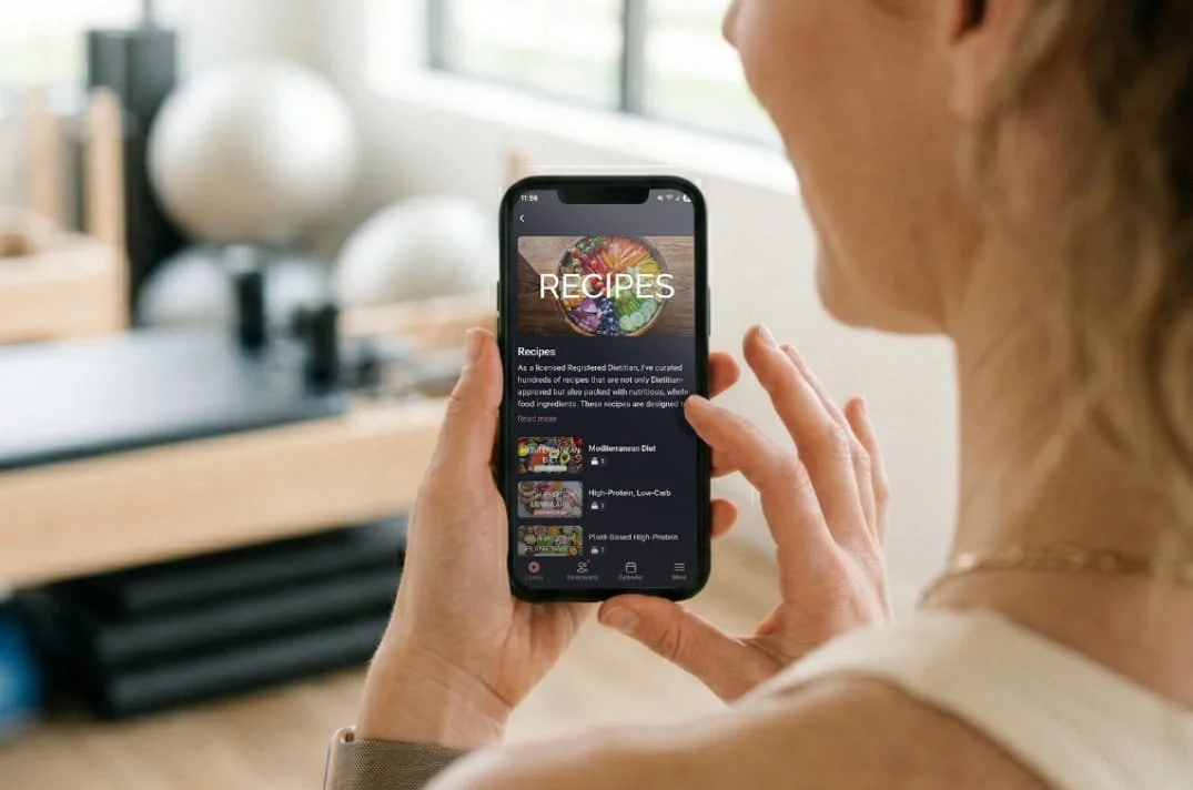 Person holding smartphone displaying a recipes app in a bright kitchen.