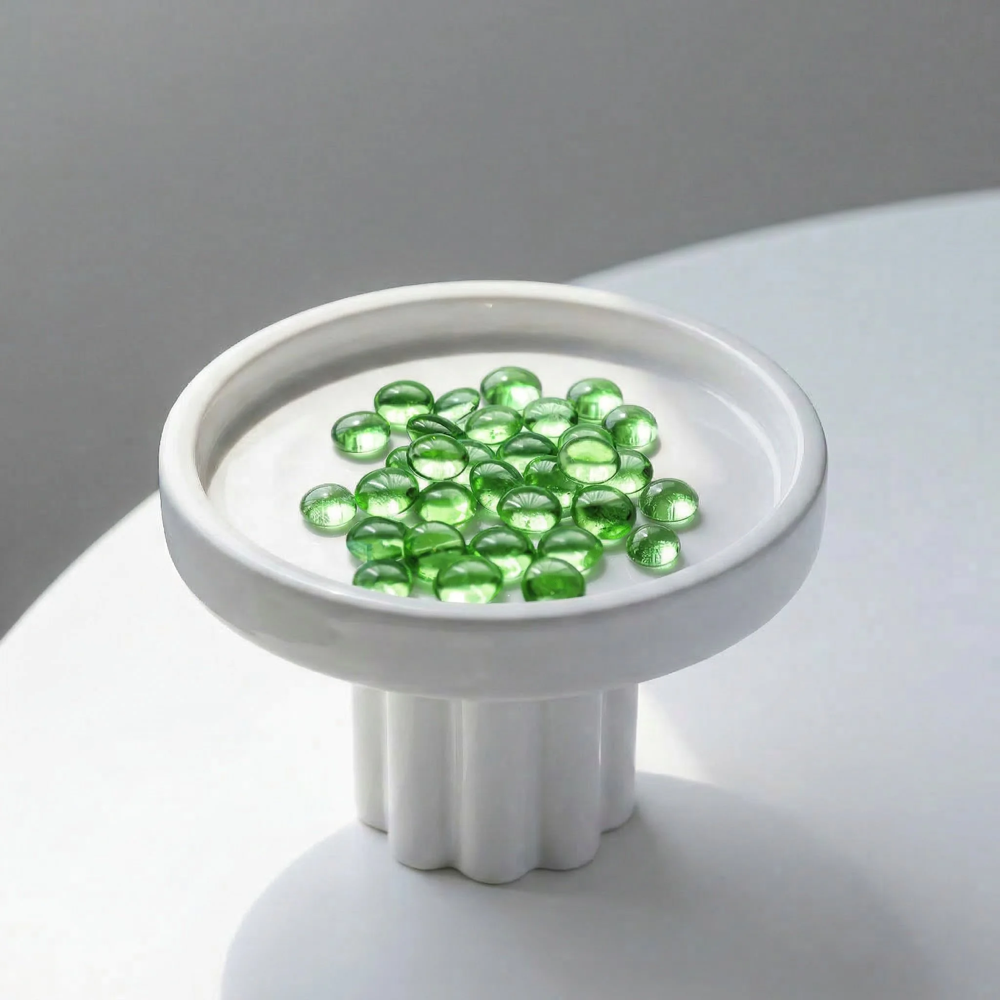 Green glass marbles in a small, white, round dish placed on a white surface.