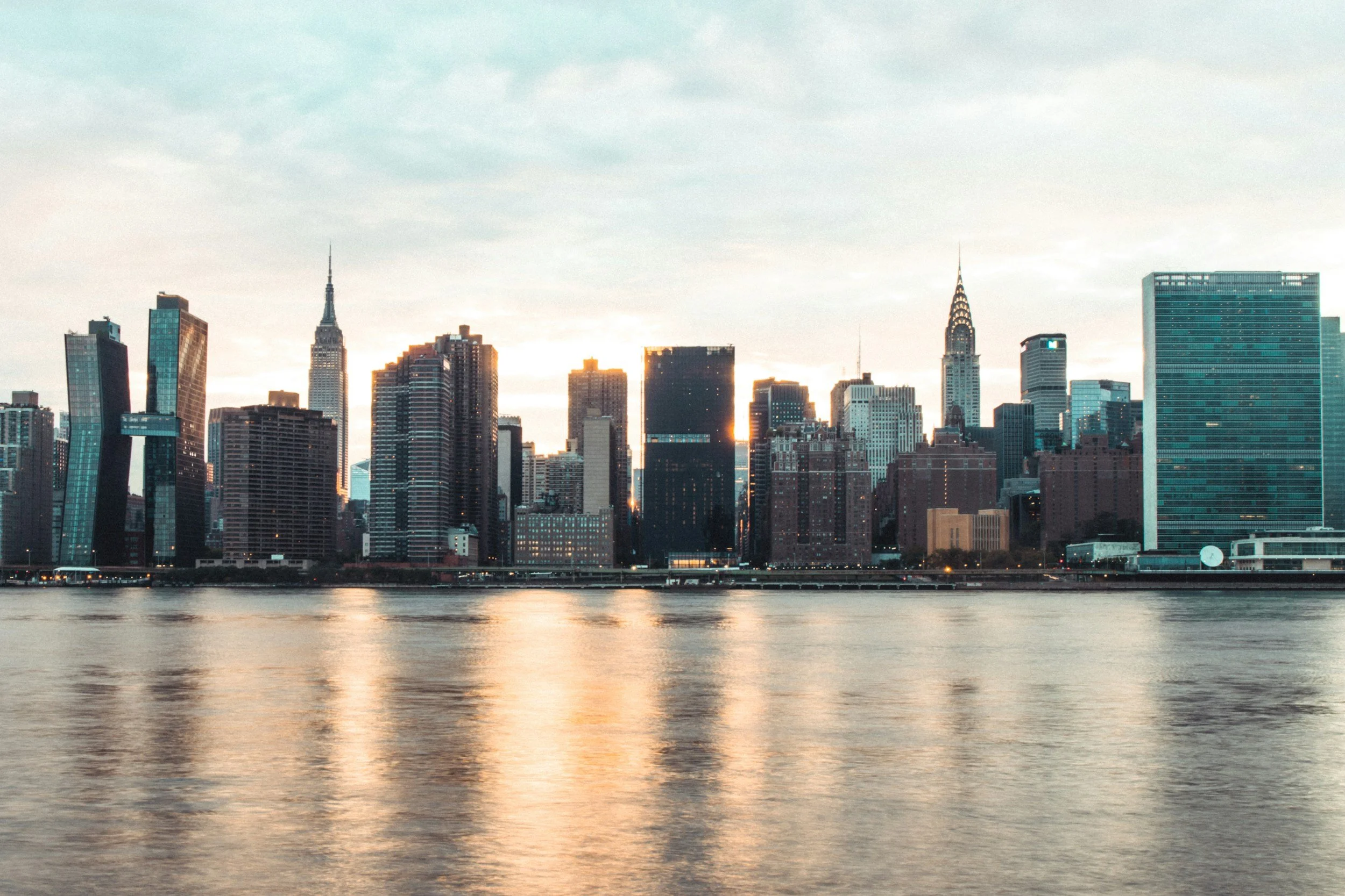 City skyline with tall buildings and skyscrapers viewed from across a body of water at sunset.