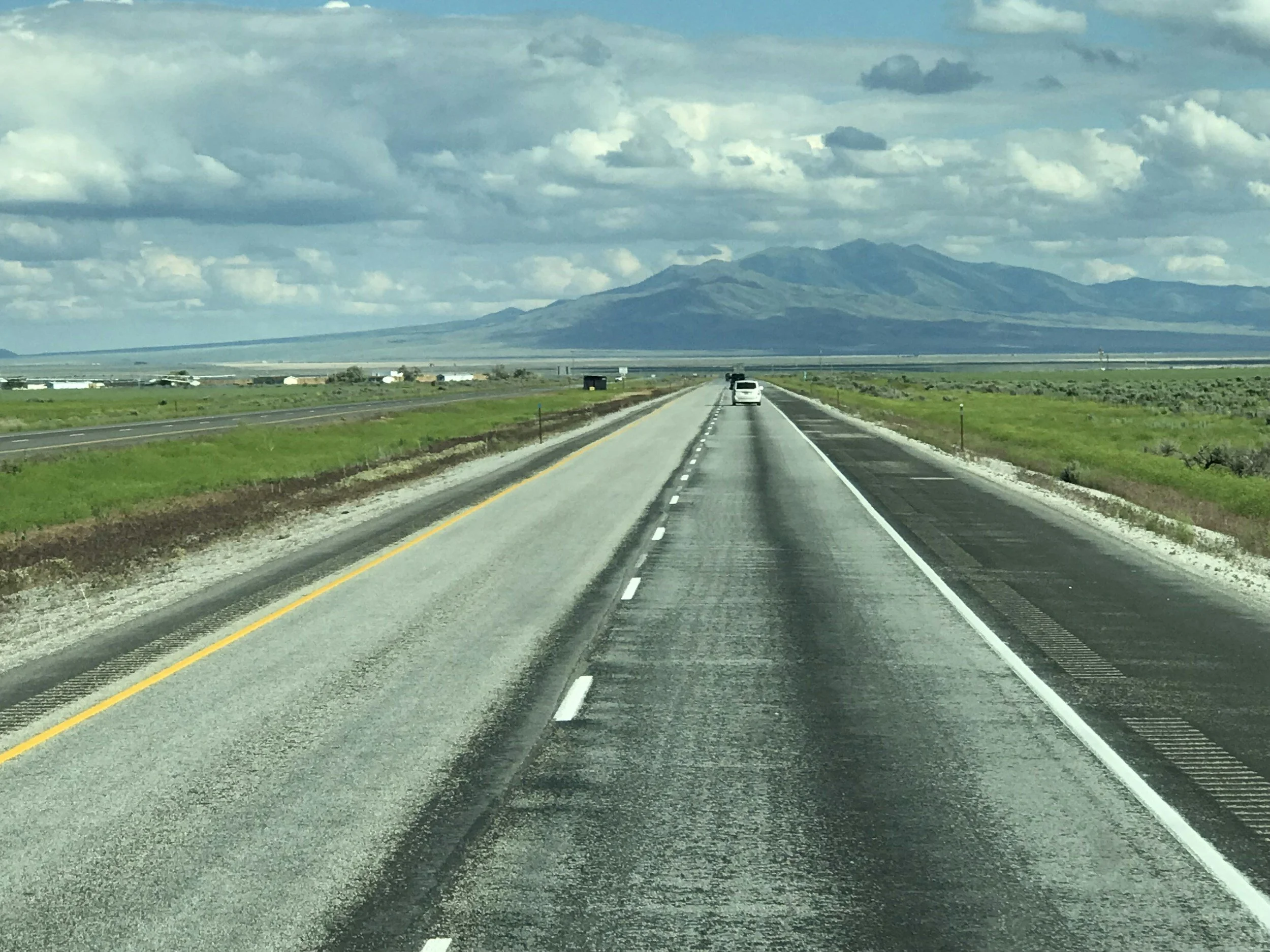 A view of a highway leading towards mountains in the distance, with a cloudy sky overhead.