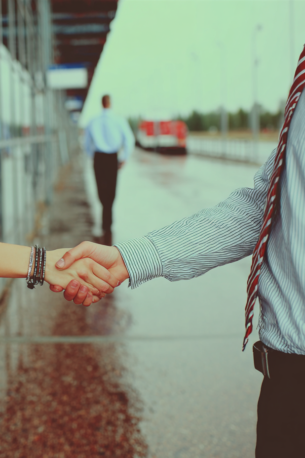 Handshake between two businesspeople outdoors, with a man in a striped shirt and red tie and a woman wearing bracelets