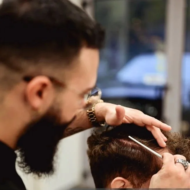 Barber performs hair thinning procedure on a client's scalp with a tool.