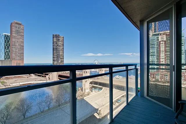 Balcony view overlooking city skyscrapers, the ocean, and a Ferris wheel in the distance on a sunny day.