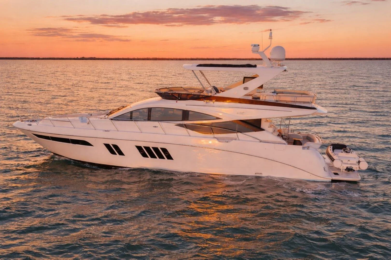 A large white luxury yacht on the water during sunset with a pink and orange sky.