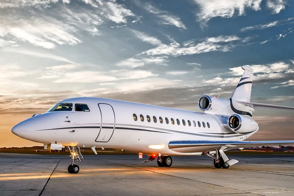 A private jet parked on an airport tarmac during sunset with a partly cloudy sky.