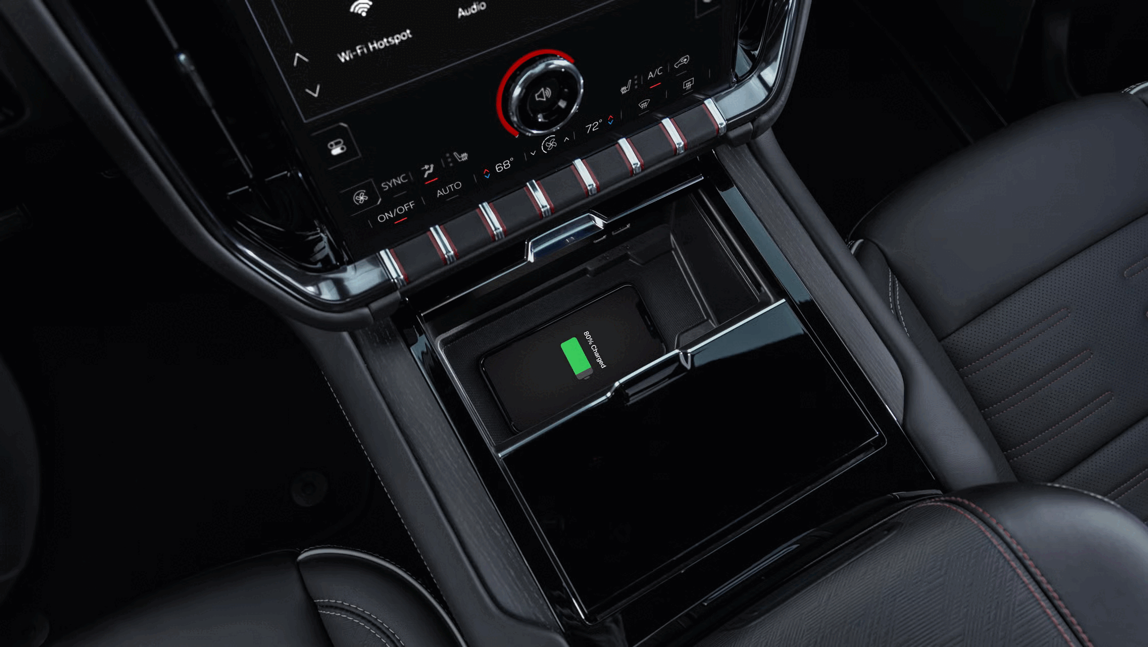 Close-up of a car's center console showing a wireless charging pad with a phone charging at 80%, climate control buttons, and a digital display.