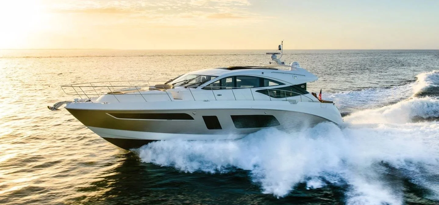 A white yacht sailing on the open ocean during sunset, creating waves as it moves at high speed.