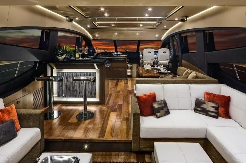Luxurious yacht interior with modern seating, a bar area, and large windows showing sunset views.