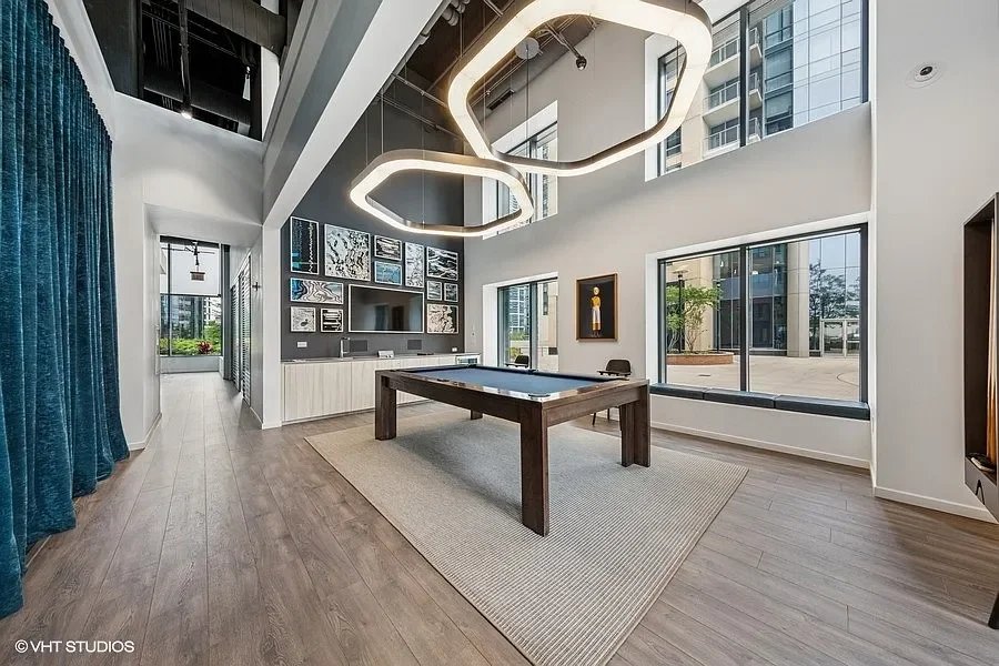 Modern game room with pool table, large windows, wall-mounted TV, artwork, and stylish lighting fixtures.