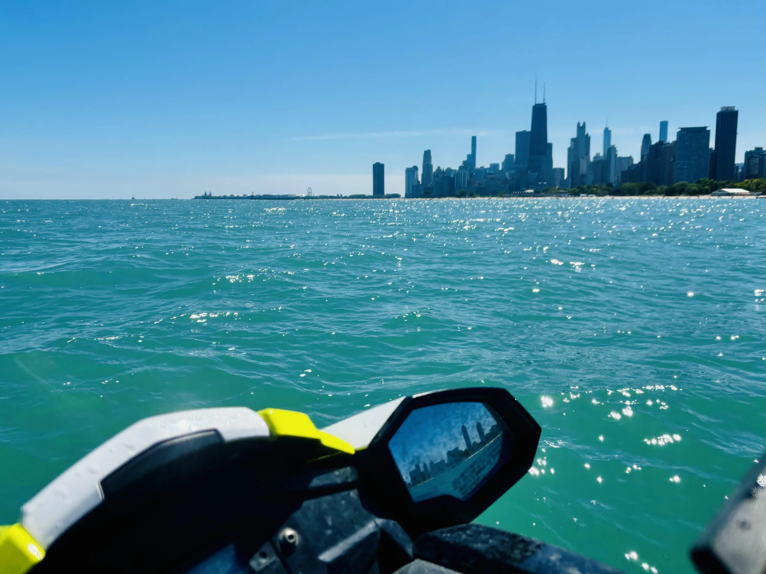 View from a boat or watercraft looking out over turquoise water toward a city skyline with skyscrapers under a clear blue sky.